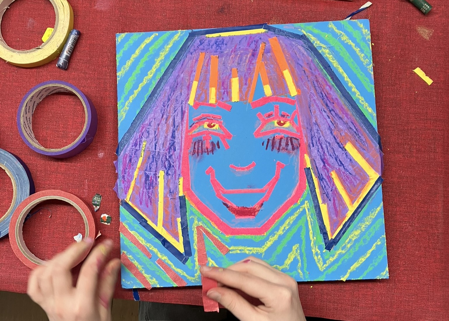 Blick auf ein buntes Kunstwerk, das ein Selbstportrait aus bunten Kreiden und Klebebändern auf blauem Untergrund zeigt.